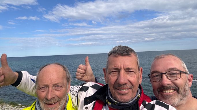 Tourguide mit zwei zufriedenen Teilnehmern am Zielpunkt des ACT Italien mit Meer im Hintergrund