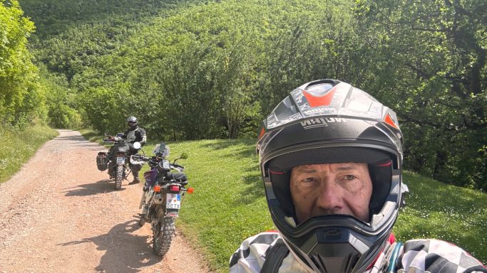 Tourguide Mike Caspers mit Teilnehmer und zwei Motorrädern auf einem Schotterweg des ACT Italien